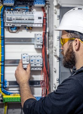 Male electrician at the checkout counter on a blurred background of a switchboard.