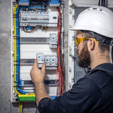 Male electrician at the checkout counter on a blurred background of a switchboard.