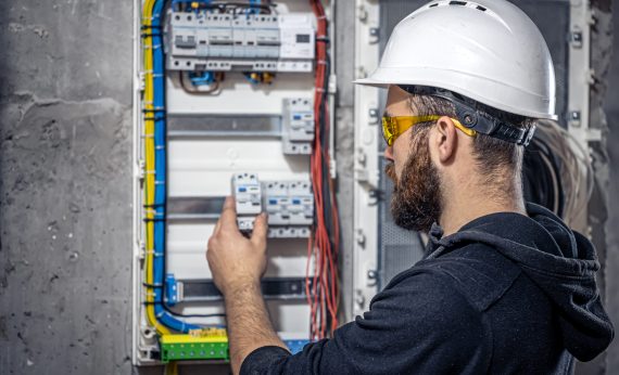 Male electrician at the checkout counter on a blurred background of a switchboard.