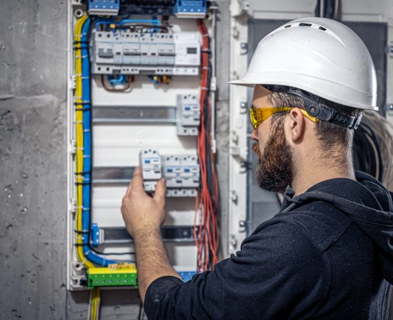 Male electrician at the checkout counter on a blurred background of a switchboard.