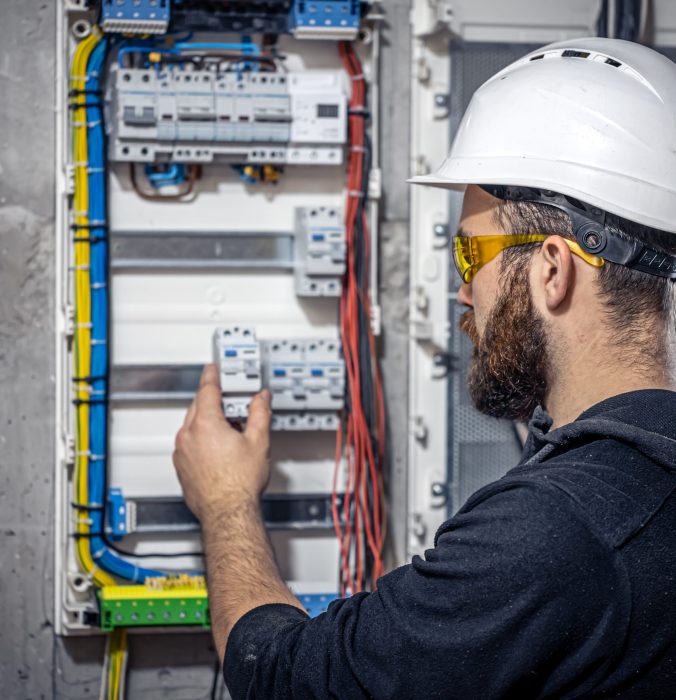 Male electrician at the checkout counter on a blurred background of a switchboard.
